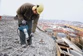 Seseorang yang mengenakan peralatan keselamatan menggunakan palu pembongkaran untuk memecahkan beton di atap.