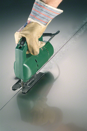 Orang yang mengenakan perlengkapan keselamatan menggunakan gergaji ukir untuk memotong garis lurus pada logam.