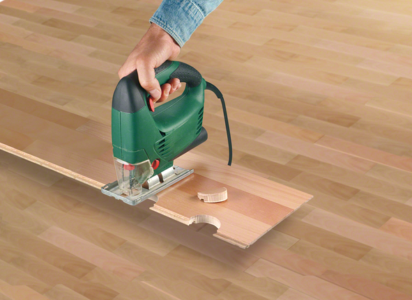 Seseorang menggunakan gergaji ukir untuk membuat lekukan melingkar pada papan kayu.