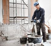 Seseorang yang mengenakan peralatan keselamatan mencampur material konstruksi dengan mekanisme pengadukan.