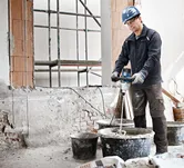 Seseorang yang mengenakan peralatan keselamatan mencampur material konstruksi dengan mekanisme pengadukan.