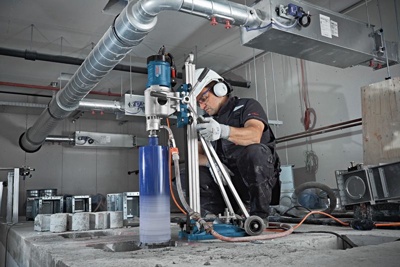 Seseorang yang mengenakan peralatan keselamatan mengoperasikan bor inti di lantai beton.