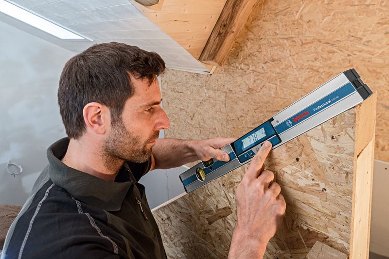 Seseorang menggunakan inclinometer digital untuk mengukur sudut struktur kayu.