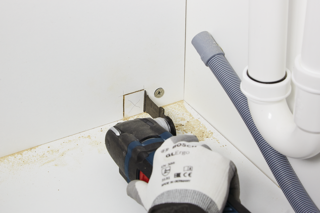 Pekerja yang mengenakan peralatan keselamatan memotong lubang persegi pada lemari dengan perkakas listrik.