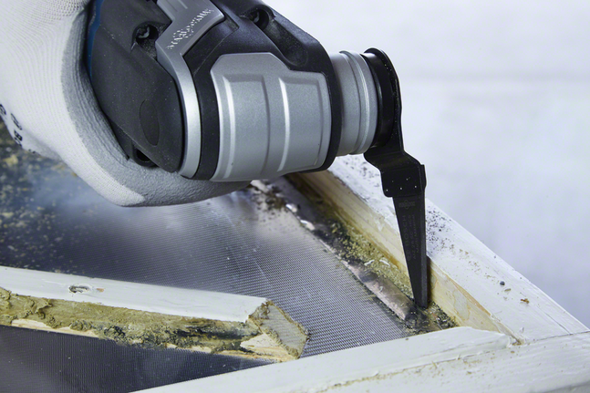 Tangan bersarung tangan menggunakan alat osilasi untuk memotong dempul bingkai jendela lama.