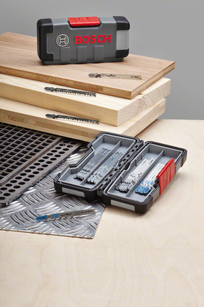 Set mata gergaji jigsaw dipajang di atas lembaran kayu dan logam, dengan mata gergaji tersusun rapi di dalam wadah.