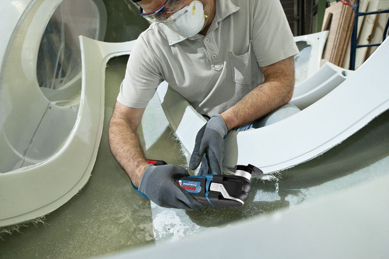 Seseorang yang mengenakan perlengkapan keselamatan memotong fiberglass dengan alat multiguna tanpa kabel.