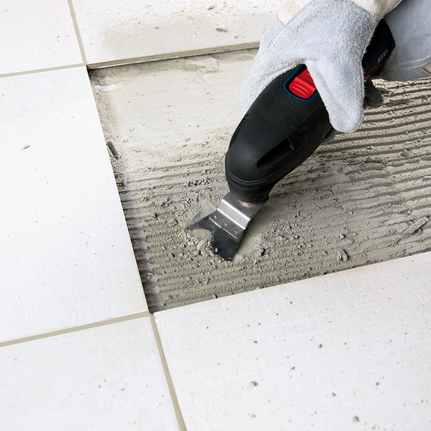 Seseorang yang mengenakan peralatan keselamatan menggunakan alat listrik untuk menghilangkan perekat di bawah ubin lantai.