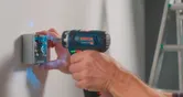 Seseorang menggunakan bor tanpa kabel untuk mengencangkan sekrup ke kotak listrik di dinding.