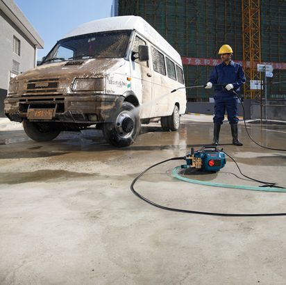 GHP 5-13 C Seseorang yang mengenakan perlengkapan keselamatan menggunakan mesin cuci bertekanan tinggi untuk membersihkan mobil van yang kotor.