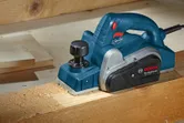 Planer listrik menghaluskan papan kayu di meja kerja.
