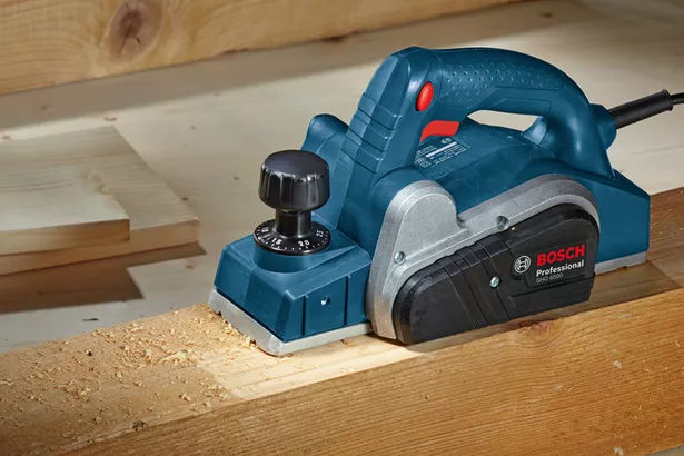 GHO 6500 Planer listrik menghaluskan papan kayu di meja kerja.