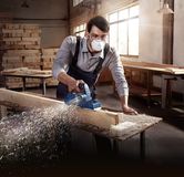 Seseorang yang mengenakan perlengkapan keselamatan menghaluskan balok kayu dengan planer listrik.