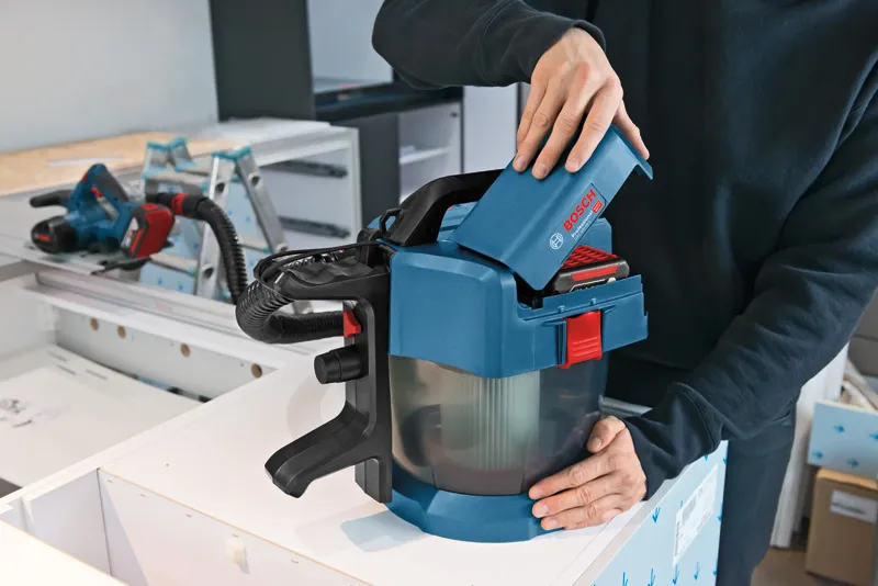 Seseorang memasukkan baterai ke dalam penyedot debu nirkabel di meja kerja.