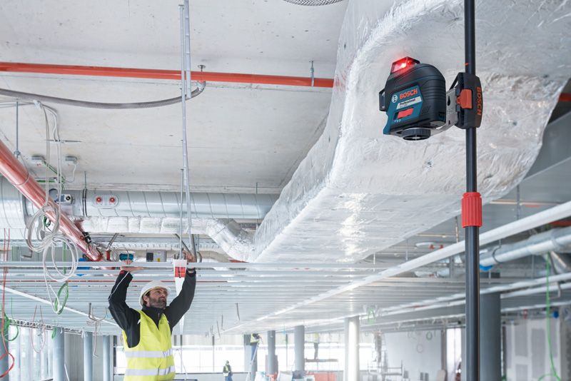 Seseorang yang mengenakan perlengkapan keselamatan menyelaraskan rangka langit-langit menggunakan alat perata laser.