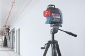 Alat perataan laser memproyeksikan garis merah melintasi langit-langit saat seseorang bekerja di tangga.