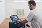 Seseorang menganalisis data kamera termal pada laptop di ruangan dengan radiator.