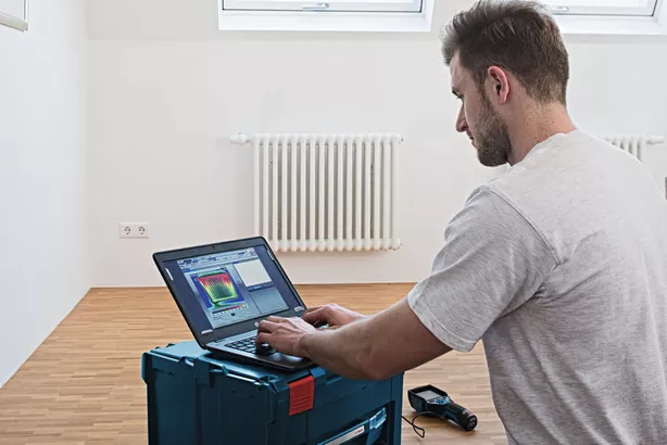 GTC 400 C Seseorang menganalisis data kamera termal pada laptop di ruangan dengan radiator.