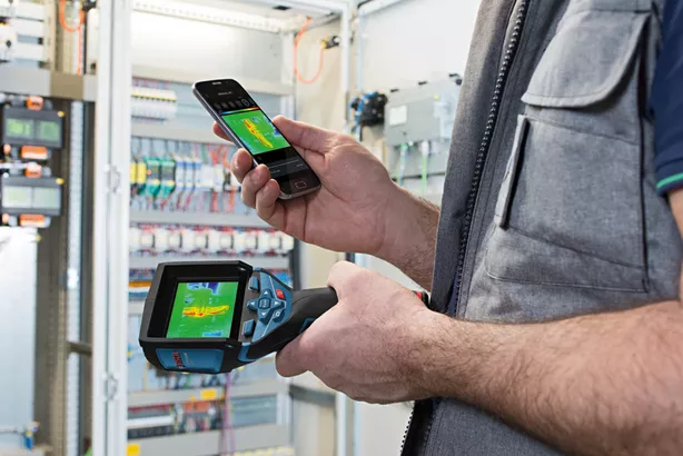 GTC 400 C Seseorang menggunakan kamera termo dan telepon pintar untuk memeriksa pola panas di panel listrik.