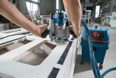 Seseorang menggunakan router listrik untuk membentuk panel kayu di bengkel.