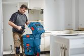 Seseorang membuka kotak penyimpanan peralatan berwarna biru dengan bor di dapur yang sedang direnovasi.