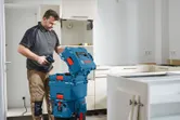 Seseorang membuka kotak penyimpanan peralatan berwarna biru dengan bor di dapur yang sedang direnovasi.