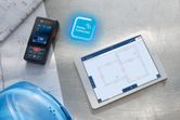 Pengukuran laser pada cetak biru di samping tablet digital yang menampilkan rencana bangunan.