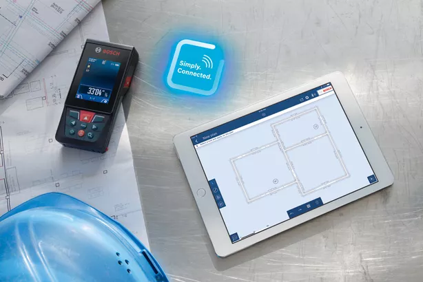 GLM 150 C Pengukuran laser pada cetak biru di samping tablet digital yang menampilkan rencana bangunan.