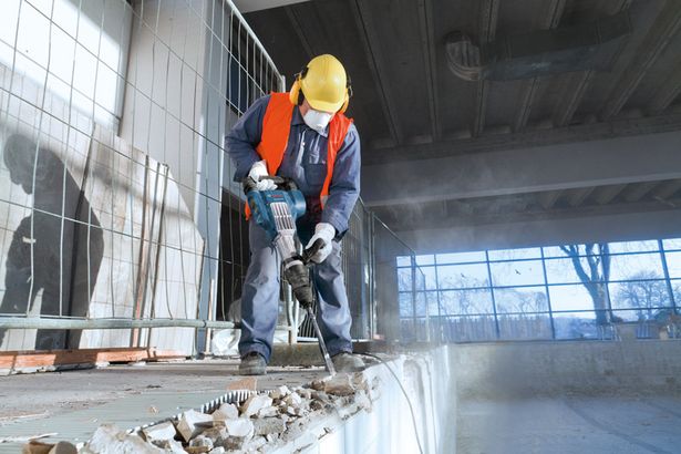 GSH 11 VC Seseorang yang mengenakan peralatan keselamatan menggunakan palu pembongkaran untuk memecahkan beton di dalam ruangan.