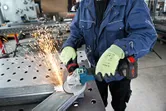 Seseorang yang mengenakan peralatan keselamatan menggiling logam dengan penggiling sudut, yang menghasilkan percikan api.