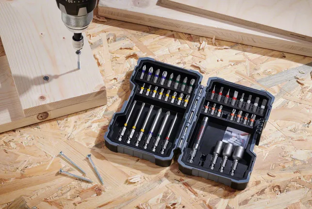 Bor listrik diletakkan di atas permukaan kayu lapis di samping sekrup dan papan kayu.