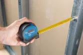 Seseorang menggunakan pita pengukur untuk memeriksa jarak antara drywall dan rangka logam.