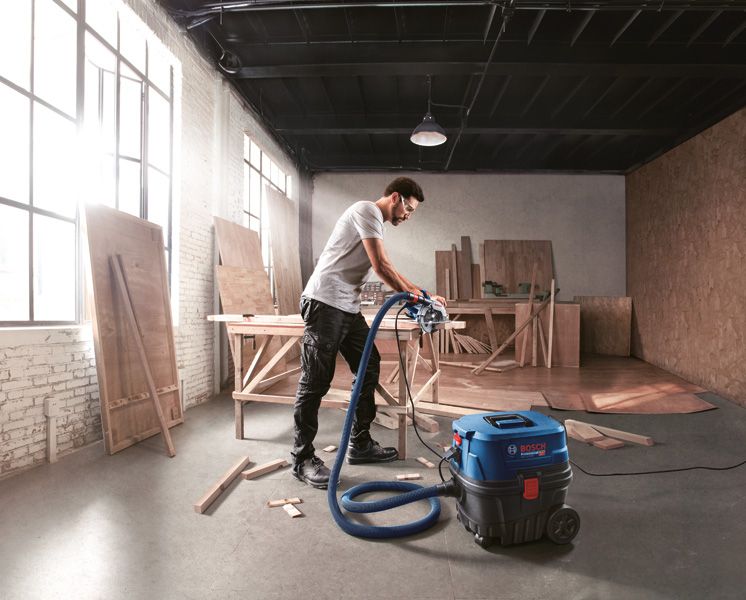 Seseorang yang mengenakan perlengkapan keselamatan menggunakan penyedot debu di bengkel kayu.