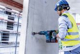 Orang yang mengenakan peralatan keselamatan mengebor dinding beton dengan palu putar tanpa kabel.
