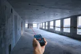 Seseorang menggunakan pengukur laser untuk menentukan jarak di ruangan beton yang belum selesai.