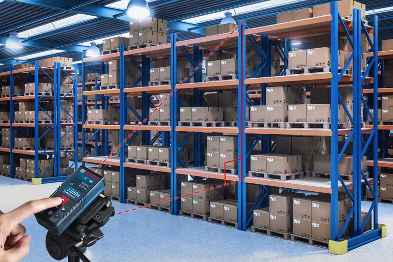 Seseorang menggunakan pengukur laser untuk memeriksa jarak antar rak gudang.