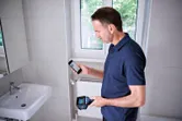 Seseorang menggunakan kamera termal dan telepon pintar di kamar mandi keramik.