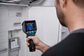 Seseorang menggunakan kamera termo untuk memeriksa panel listrik.
