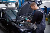 Seseorang yang mengenakan peralatan keselamatan memeriksa mesin mobil dengan kamera termo.