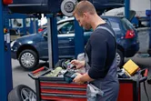Seseorang yang mengenakan perlengkapan keselamatan menggunakan kamera termo saat bekerja di bengkel mobil.
