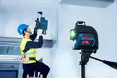 Seseorang yang mengenakan perlengkapan keselamatan mengebor langit-langit dengan panduan alat perataan laser.