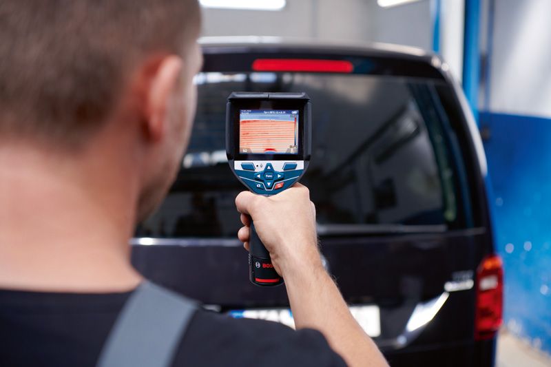 Seseorang menggunakan kamera termal untuk memindai kaca belakang sebuah van hitam.