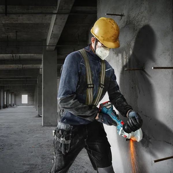 Seseorang yang mengenakan peralatan keselamatan memotong beton dengan penggiling sudut.