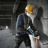 Seseorang yang mengenakan peralatan keselamatan memotong beton dengan penggiling sudut.