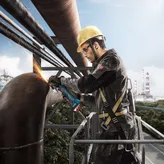 Seseorang yang mengenakan peralatan keselamatan menggiling pipa logam besar dengan penggiling sudut.