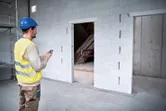 Orang yang mengenakan peralatan keselamatan menggunakan pengukur laser untuk memeriksa dimensi pintu di lokasi konstruksi.