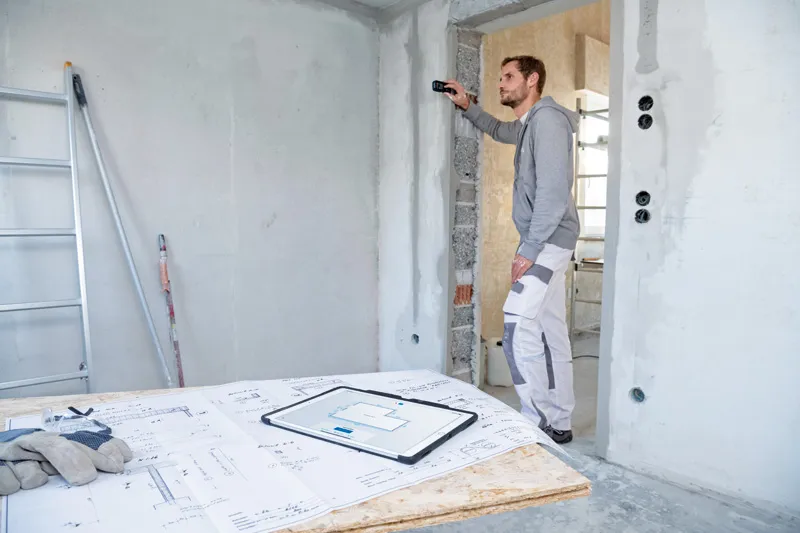 GLM 50-27 CG Seseorang menggunakan pengukur laser untuk memeriksa jarak dinding di lokasi konstruksi.