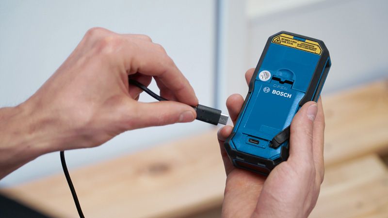 Seseorang menyambungkan kabel pengisi daya ke bagian belakang perkakas listrik genggam.