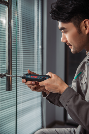 Seseorang mengencangkan sekrup pada gagang pintu kaca menggunakan obeng tanpa kabel.