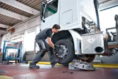 Orang yang mengenakan peralatan keselamatan menggunakan kunci pas benturan untuk mengencangkan baut pada roda truk.